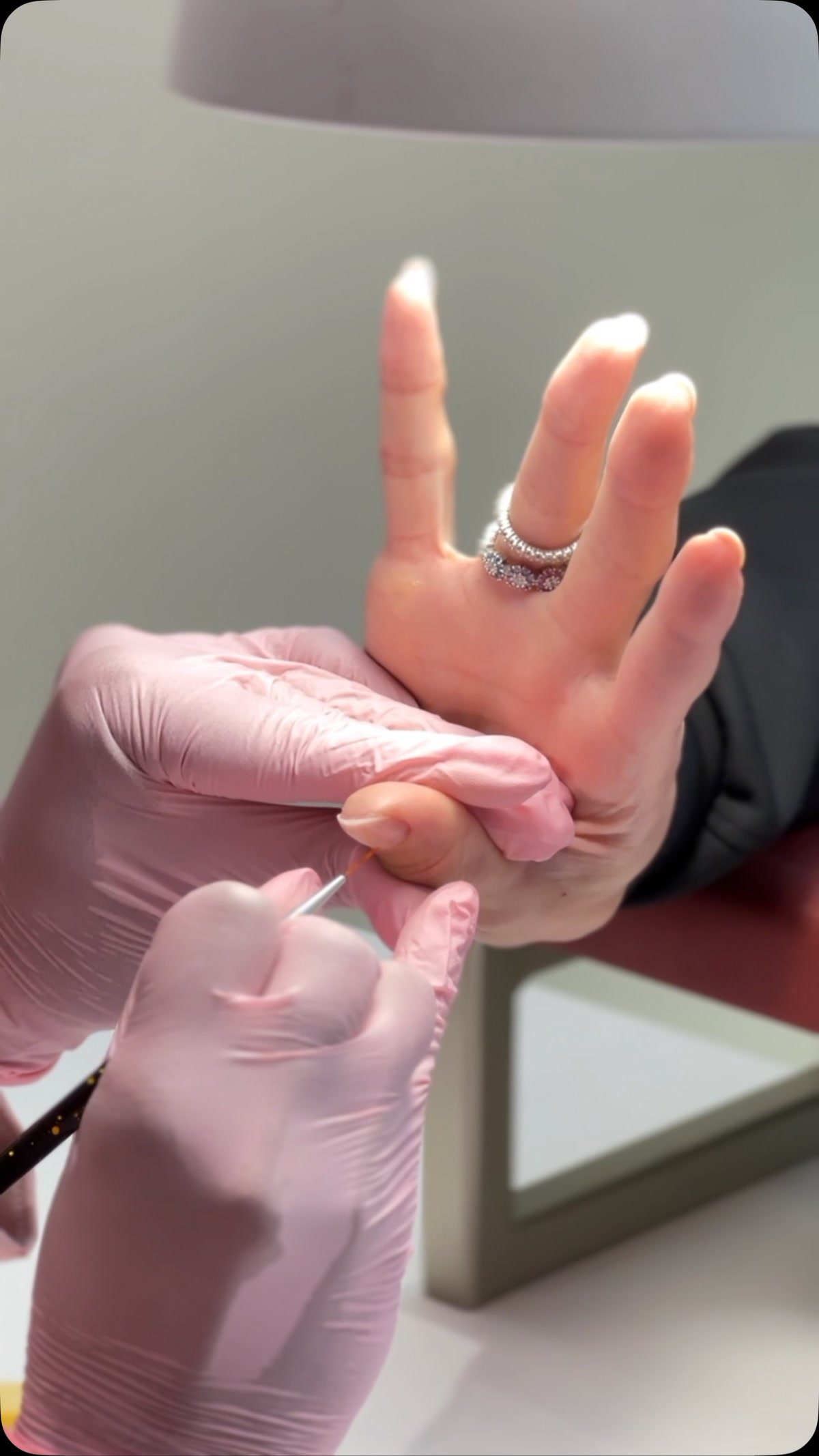 Mãos com luva rosa segurando a mão de uma cliente, com a unha natural sem esmalte, antes do preparo