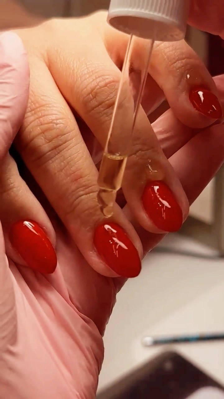 Produto sendo aplicado sobre unhas naturais em vermelho intenso, com acabamento espelhado